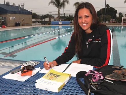 lauren smiling to the camera in front of the pool writing on a book.